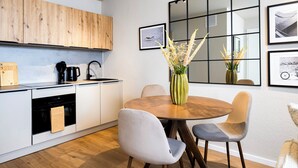 Une cuisine moderne avec des meubles en bois, un coin repas doté d’une table ronde et de chaises, et des œuvres d’art encadrées accrochées aux murs.
