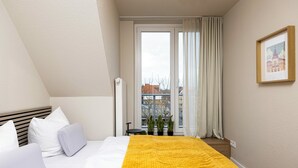 Une chambre à coucher avec un lit, des oreillers blancs, une couverture jaune, une fenêtre avec des rideaux et un tableau encadré accroché au mur.