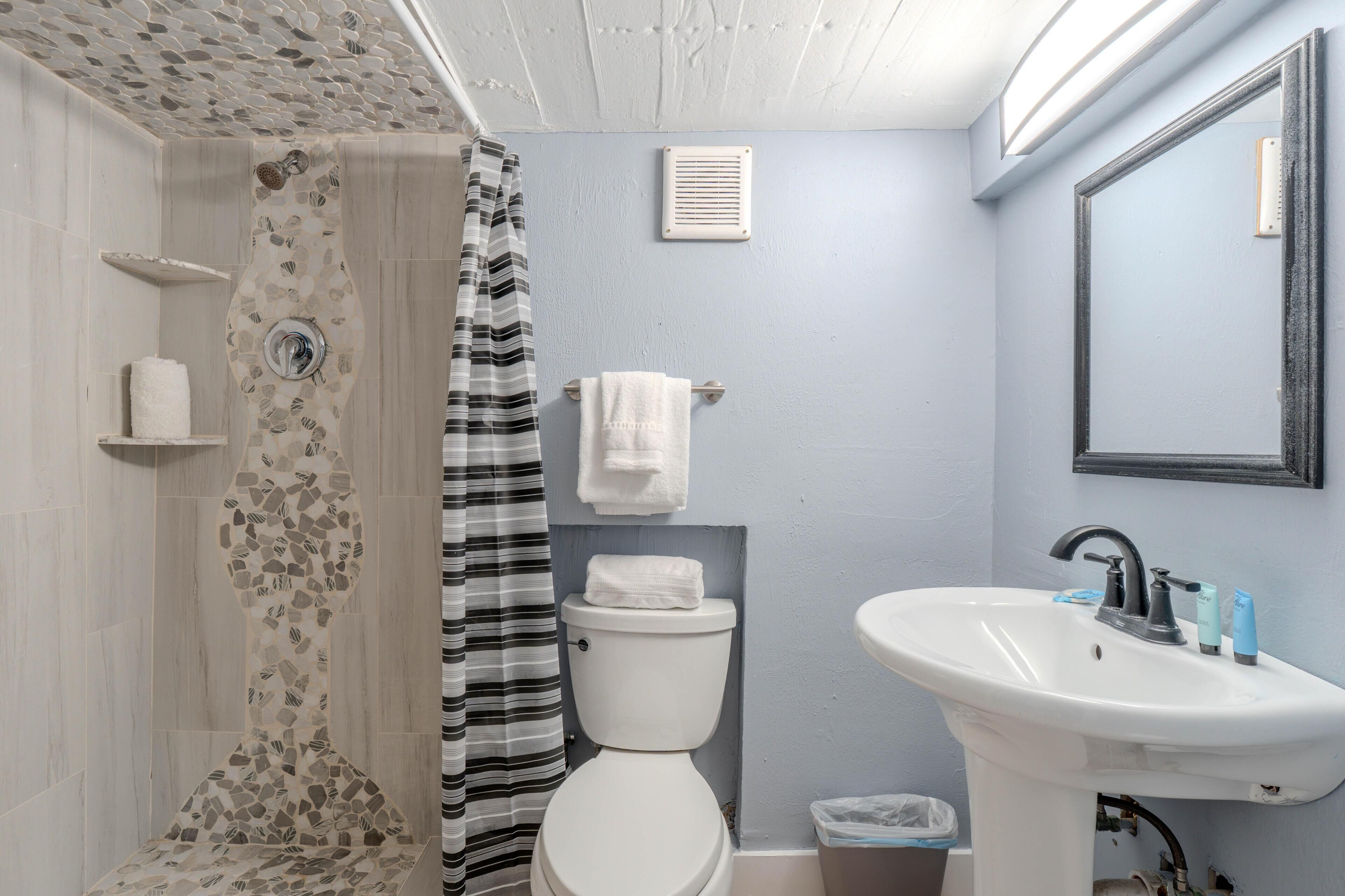 A bathroom with a shower, toilet, sink, and a mirror.