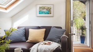 A cozy living room with a leather sofa, a framed painting, and a potted plant. - Cornwall Getaway for two - The Loft (Saint Kew)