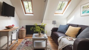 A cozy loft apartment with a high ceiling, two skylights, a brown leather sofa, a white table, and a black radiator. - Cornwall Getaway for two - The Loft (Saint Kew)