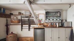 A kitchen with wooden cabinets, a stainless steel dishwasher, and a wooden dining table. - Cornwall Getaway for two - The Loft (Saint Kew)