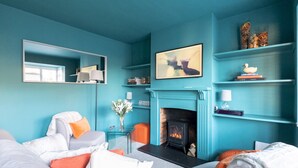 Ein salbeigrün-farbenes Wohnzimmer mit Kamin, einer Couch, einem Couchtisch und einem Bücherregal.