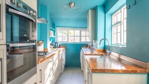 Eine Küche mit türkisfarbenen Wänden, einem Edelstahlbackofen, Holz Arbeitsplatten und einem Fenster mit weißen Rahmen.