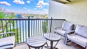 A balcony with a view of a beach and resort area, featuring a sofa, two round tables, and a railing. - Land's End 3-403 Bay Front - Premier (Treasure Island)