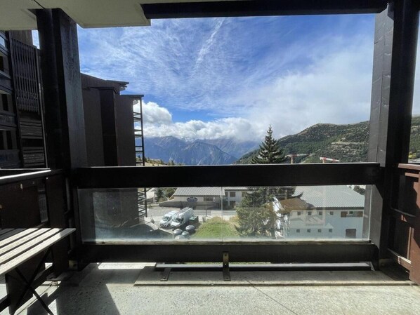 A balcony with a view of mountains, a building, and parked vehicles.
