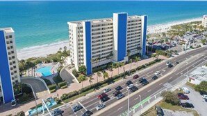 A beachfront hotel with multiple floors, a swimming pool, and a road with parked cars.