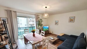 A living room with a sofa, a dining table with chairs, a TV, and a balcony with a view of buildings. - Charming T3 with balconies in Ajaccio (Ajaccio)