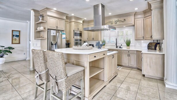 A spacious kitchen with light wood cabinets, a stainless steel range hood, and a central island with seating.
