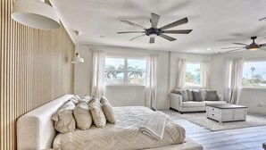 A modern bedroom with a large bed, a sofa, a coffee table, and two ceiling fans.