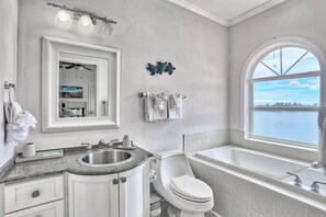 A modern bathroom with a large window, a bathtub, a sink, and a toilet. - Villa At Bahia Shores-whole Property (St. Pete Beach)