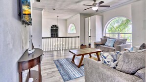 A spacious living room with a wooden coffee table, grey sofa, and a ceiling fan.