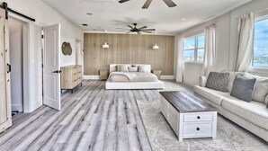 A modern bedroom with a large bed, a sofa, a coffee table, and a ceiling fan.
