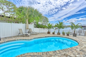 A swimming pool with a curved edge, surrounded by a stone patio and a white fence. - Villa At Bahia Shores-4br (St. Pete Beach)