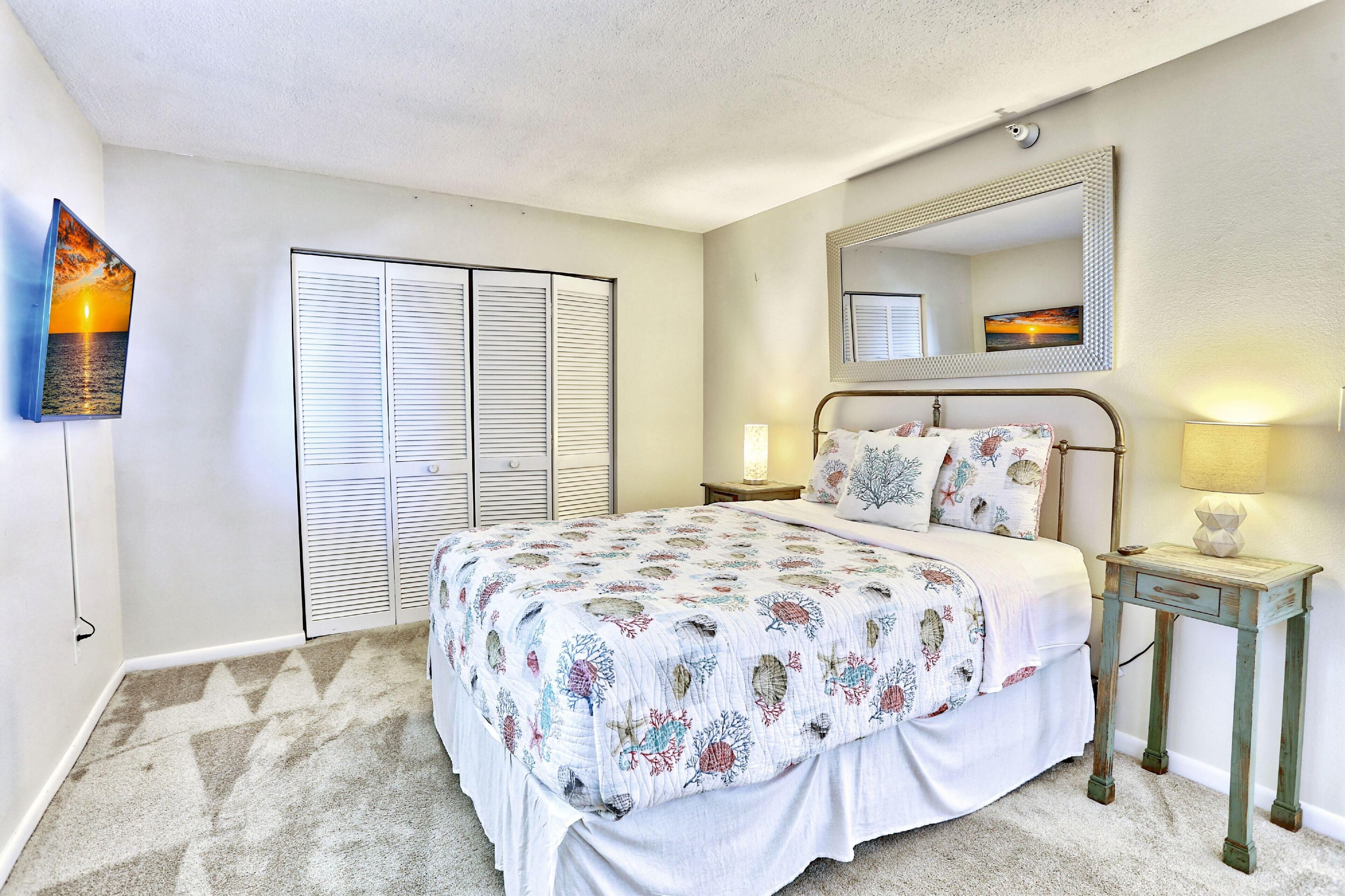 A bedroom with a bed, a nightstand, a lamp, a mirror, and a closet with sliding doors.