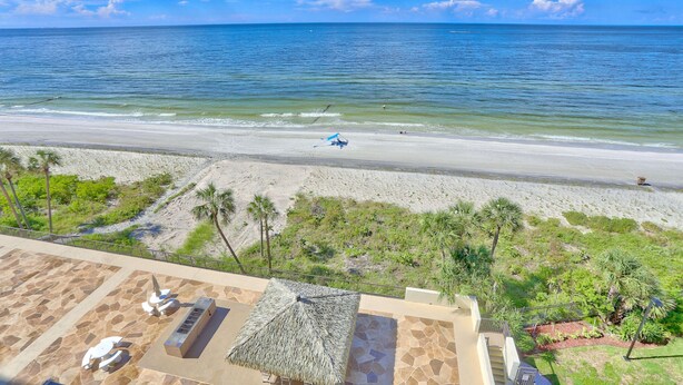 Een uitzicht op het strand vanaf een resort, met een zwembad, palmbomen en een heldere lucht.