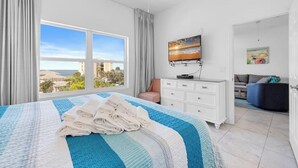 A hotel room with a large bed, a dresser, a TV, and a view of the city. - Madeira Bay Resort I 1402 (Madeira Beach)