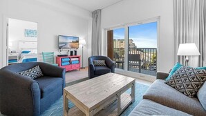 A modern living room with a sofa, armchairs, a coffee table, and a TV. There is a balcony with a view of buildings. - Madeira Bay Resort I 1402 (Madeira Beach)