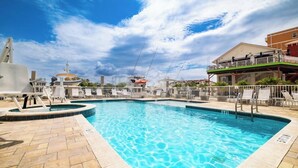 A swimming pool with a tiled deck, lounge chairs, and a building with a balcony in the background. - Madeira Bay Resort I 1402 (Madeira Beach)