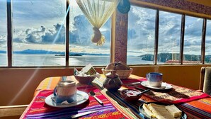 A table set with a teapot, cups, and bowls, overlooking a scenic view of mountains and a body of water. - Kalluchi Ecolodge (La Paz)