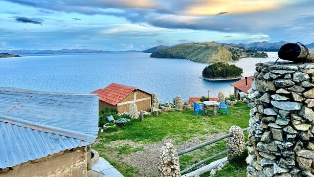 A lakeside property with a stone wall, a small building with a red roof, and a grassy area with blue chairs. - Kalluchi Ecolodge (La Paz)