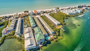 Vista aérea de un complejo turístico en la costa, con varios edificios, un puerto deportivo y aguas azules cristalinas.