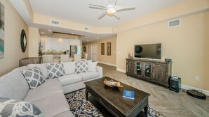 A living room with a sectional sofa, a coffee table, a TV, and a ceiling fan. - Dolphin Key 504 - Premier (Indian Shores)