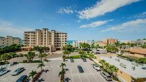 A multi-story hotel with a central courtyard, parking area, and a view of the ocean. - Dolphin Key 504 - Premier (Indian Shores)
