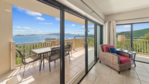 A balcony with a table and chairs, a wicker sofa, and a view of the sea and hills. - NEWLY RENOVATED! 1BR/1BA Beautiful Condo @Point Pleasant/Great views/3 Pools! (St Thomas)