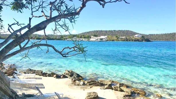 A beach with clear blue water, rocky shore, and lounge chairs. - NEWLY RENOVATED! 1BR/1BA Beautiful Condo @Point Pleasant/Great views/3 Pools! (St Thomas)