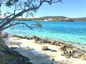 A beach with clear blue water, rocky shore, and lounge chairs.