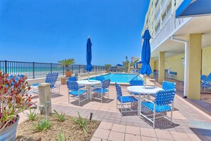 Un espace aménagé au bord de la piscine, avec des chaises et des parasols bleus, une piscine et une vue sur l’océan.