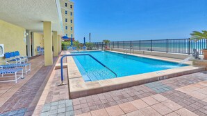 A swimming pool with a blue water feature, surrounded by a black metal fence and a tiled deck. - Tides 1-211 (North Redington Beach)