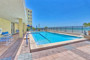 A swimming pool with a blue water feature, surrounded by a black metal fence and a tiled deck. - Tides 1-211 (North Redington Beach)