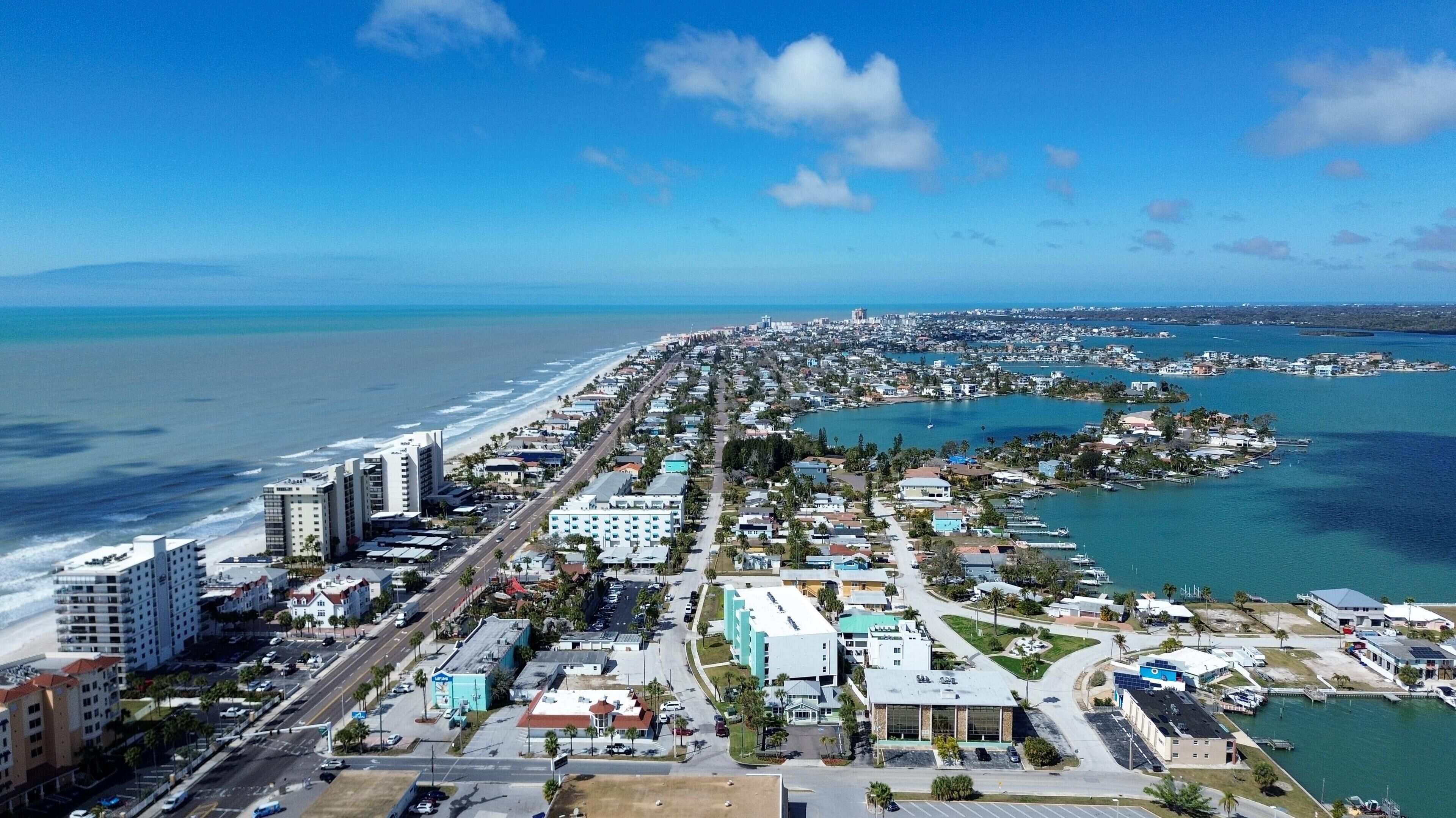 An aerial view of a coastal city with a long beachfront, dense residential area, and a marina.