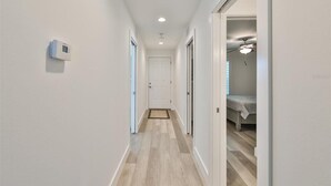 A narrow hallway with a white door at the end, leading to a bedroom with a bed and a ceiling fan. - Madeira Del Mar 301 (Madeira Beach)