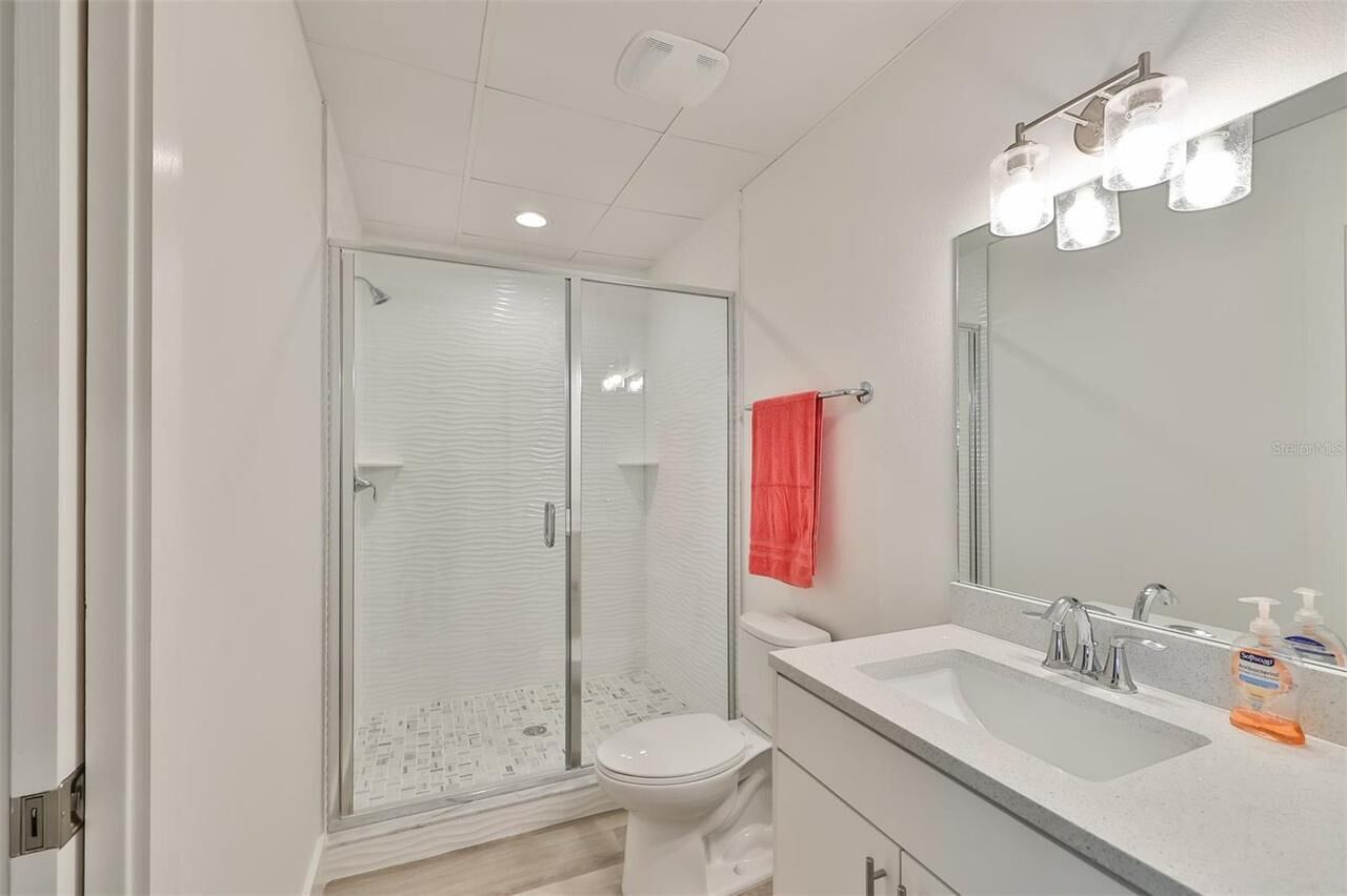 Un baño moderno con cabina de ducha de vidrio, inodoro blanco, lavabo con espejo y una toalla roja colgada en la pared.