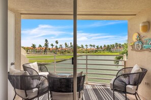 A balcony with wicker chairs, a view of a golf course, and a water body. - Vista Verde West 218 (St. Petersburg)