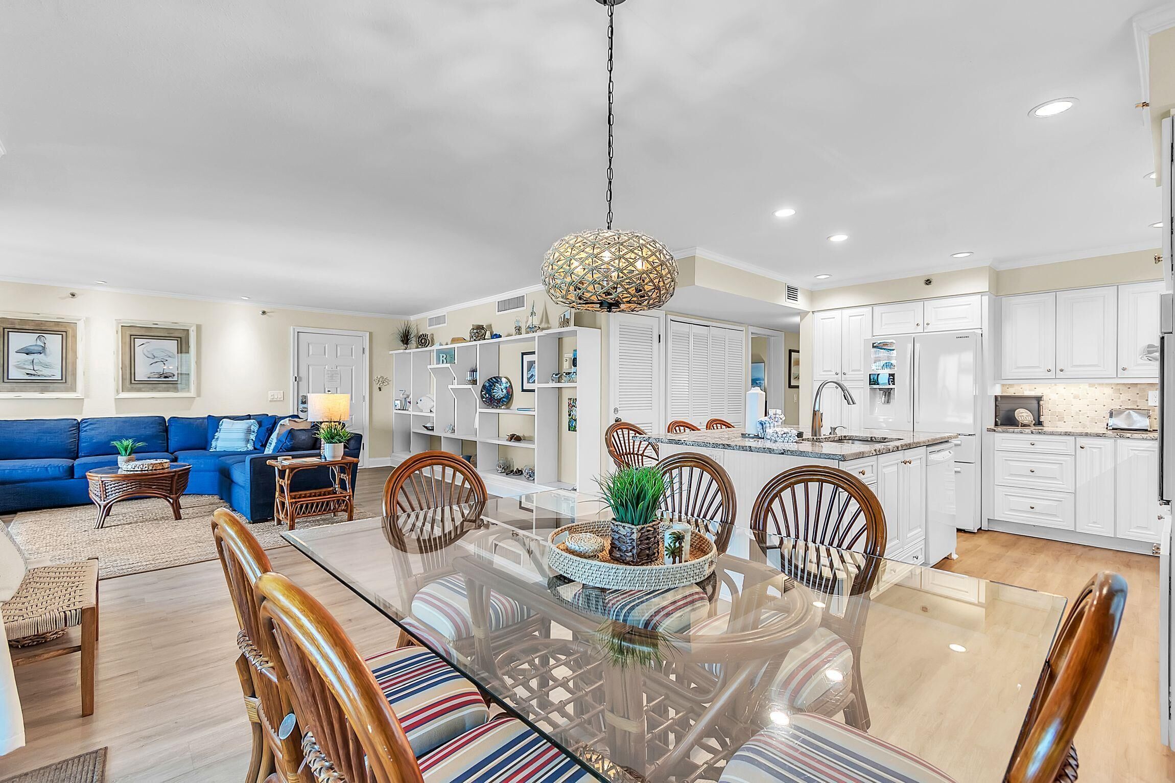 Una cocina moderna con armarios blancos, un comedor con mesa de vidrio y una sala de estar con un sofá azul.