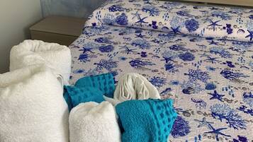 Ein Bett mit blauer und weißer Bettdecke im Meeresdesign, ein Nachttisch aus Holz und eine Kommode mit maritimer Dekoration.