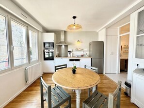 Cozinha moderna com armários brancos, uma mesa redonda de madeira e luminária pendente.