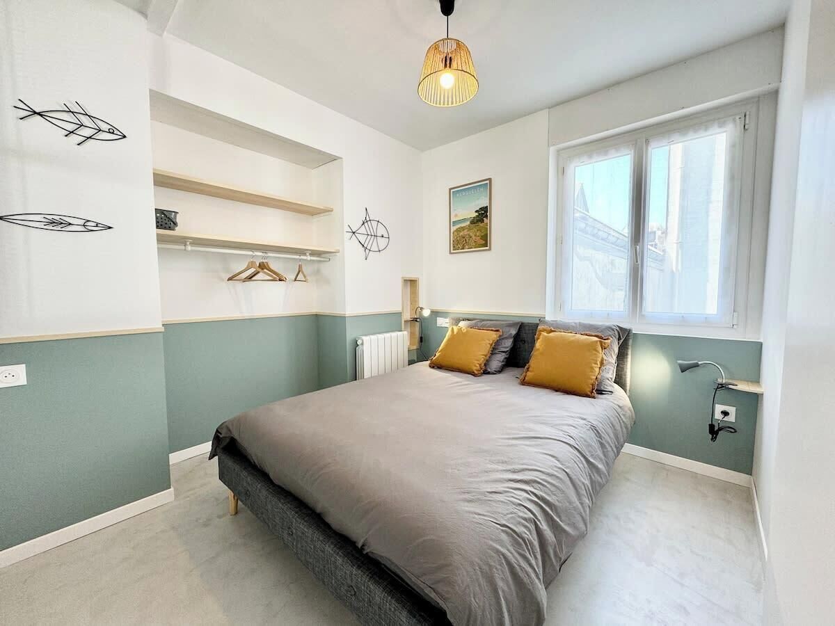 Een slaapkamer met een bed, een raam, een wandplank en een hanglamp.