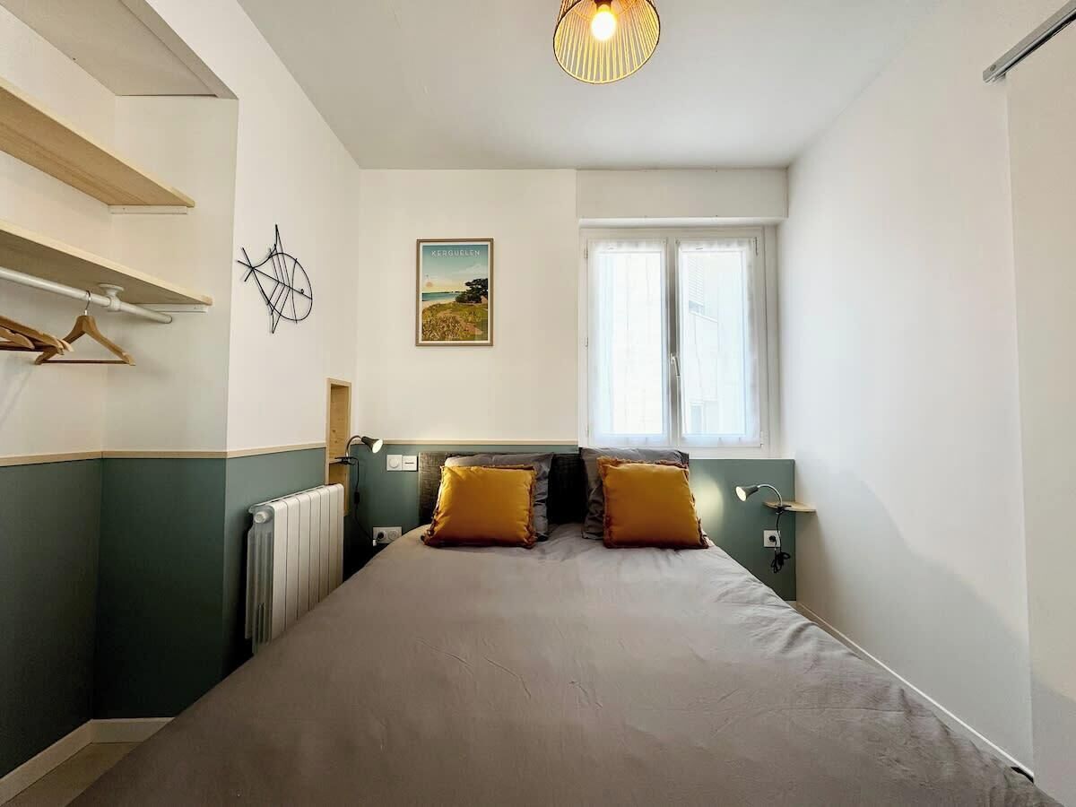 Une chambre à coucher comprenant un lit, deux oreillers, un radiateur, une fenêtre et un luminaire fixé au mur.