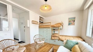 Une pièce chaleureuse avec un lit superposé, un canapé blanc agrémenté de coussins, un fauteuil en osier et une table basse en bois.