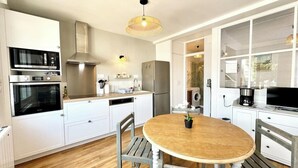 Une cuisine moderne avec des meubles blancs, une table ronde en bois et un four encastré.