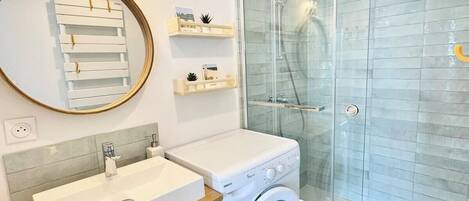 Een moderne badkamer met een glazen douche, een wastafel en een wasmachine.