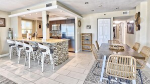 A modern kitchen with a stone island, bar stools, and a dining area with wicker chairs. - Arena De Madeira 103 - Premier (Madeira Beach)