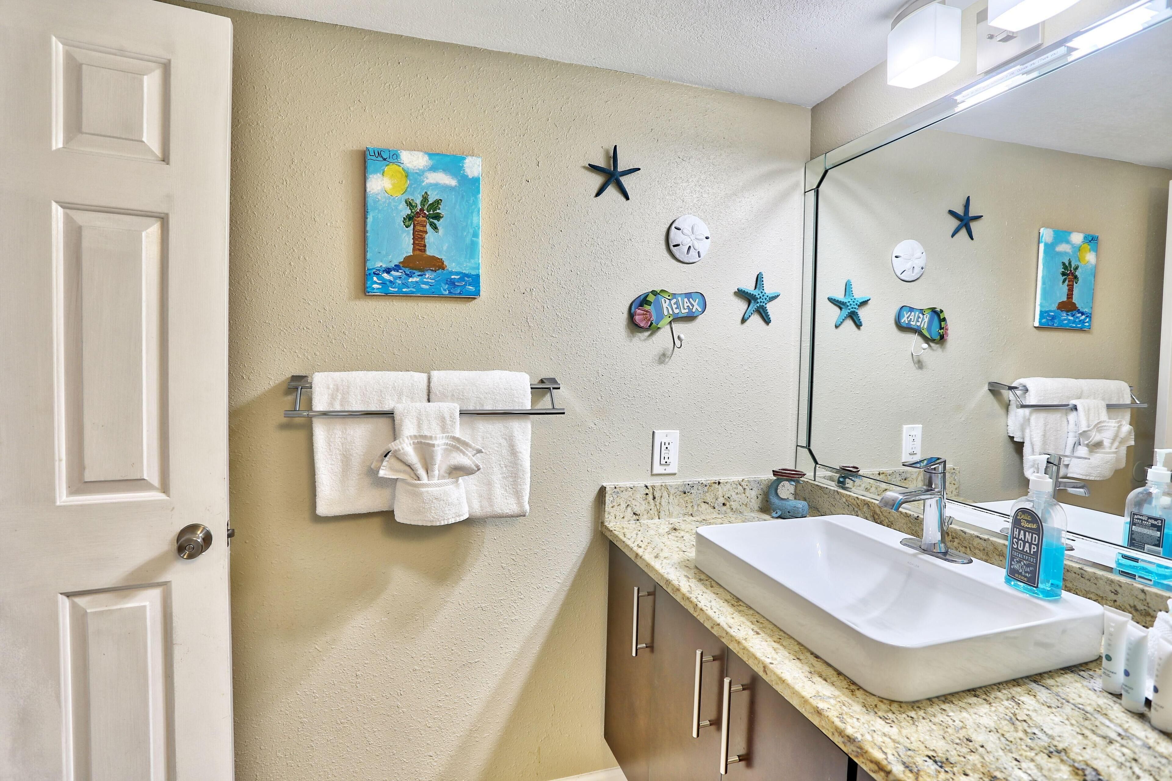 A bathroom with a white sink, a towel rack, and wall art including a palm tree painting.