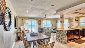 A spacious living area with a dining table, wicker chairs, and a kitchen with a stone backsplash. - Arena De Madeira 103 - Premier (Madeira Beach)