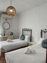 Une chambre d’hôtel avec deux lits simples, une table de chevet avec une bouilloire, un miroir et un luminaire suspendu.